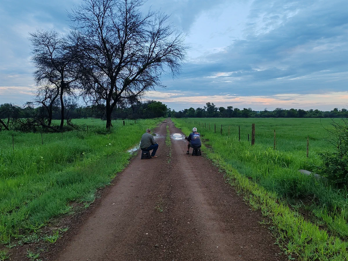 Two photographers crouched low on a dirt road at dawn, lenses pointed along the verge